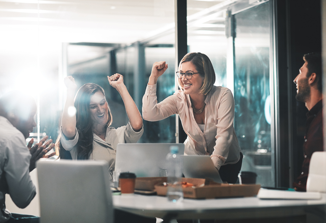 Workers in an office cheering and celebrating in front of a laptop