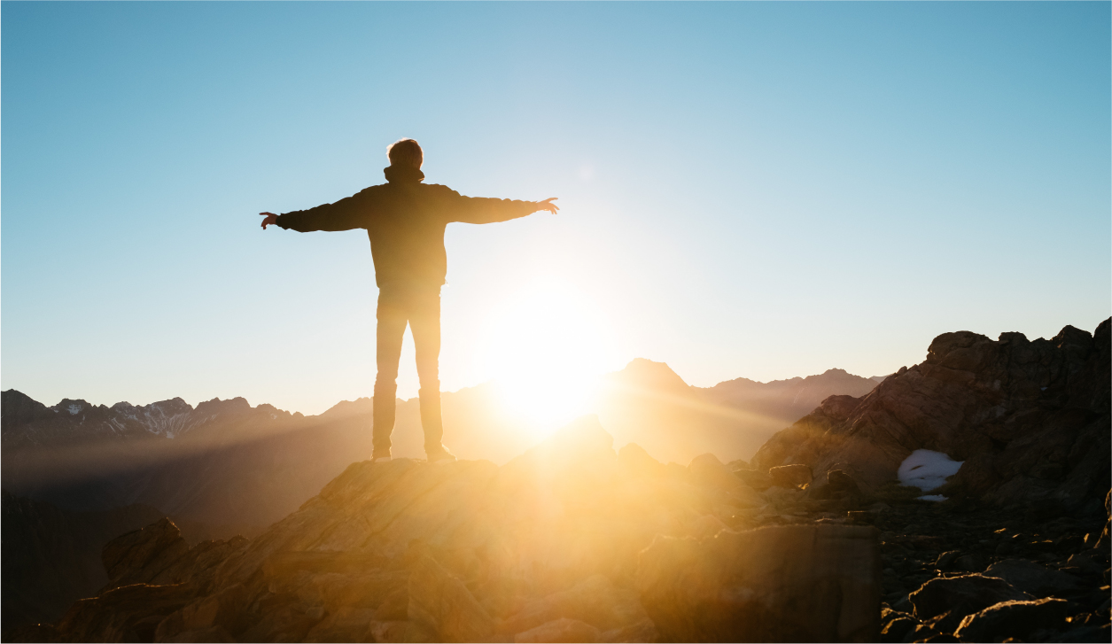 Man standing on top of a mountain in front of the sun with arms stretched wide