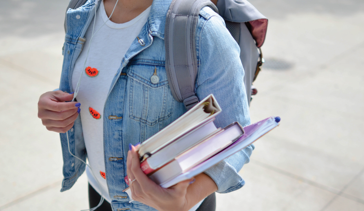 Female student holding books and a backpack on college campus